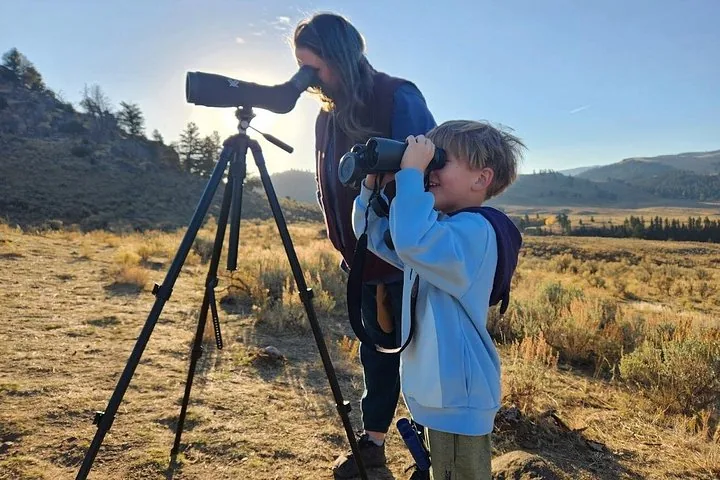 A child using binoculars next to an adult with a spotting scope